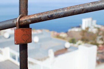 A rusty padlock with a heart pinned to a metal pipe against a blue sky