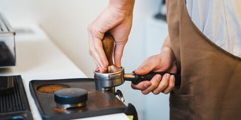 Barista using tamper in one hand while going to press ground coffee in holder