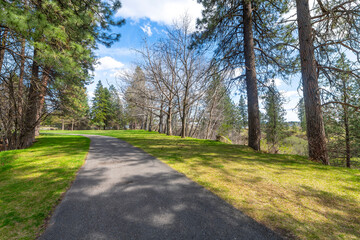 Fototapeta na wymiar Paved walking trails through the grassy areas and woods at the riverfront Plante's Ferry Park along the banks of the Spokane River in Spokane Valley, Washington, USA. 