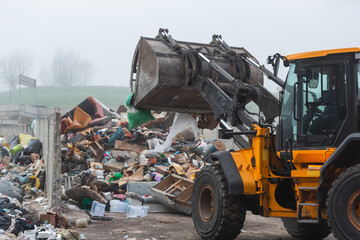 Yellow wheel loader, with lifted scrap grapple, moving along the recycling center area in process handling dumped waste