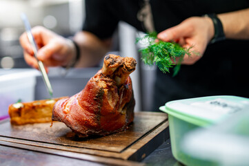 chef hand cooking Baked Pork knuckle with vegetables on plate in kitchen