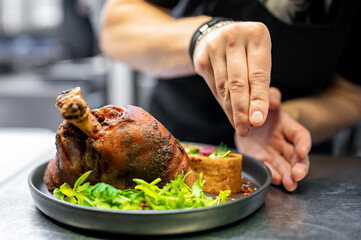 chef hand cooking Baked Pork knuckle with vegetables on plate in kitchen