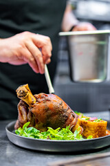 chef hand cooking Baked Pork knuckle with vegetables on plate in kitchen