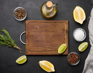 Various lemon and lime slices on a wooden board. Salt, spices and rosemary branches on a black background, top view