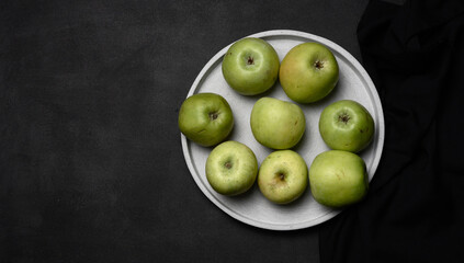 Ripe green apples on a gray plate, top view on a black wooden table