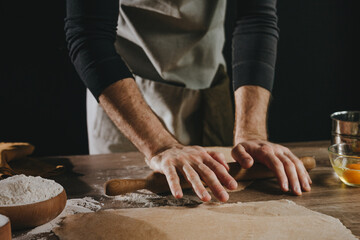 Unrecognizable man rolling out the dough with a rolling pin on wooden background