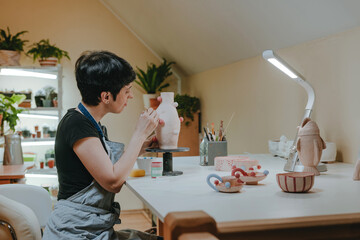 Female craft person painting a vase indoor