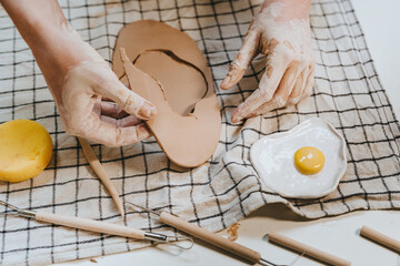 Young woman potter carving a plate from clay in her workshop.