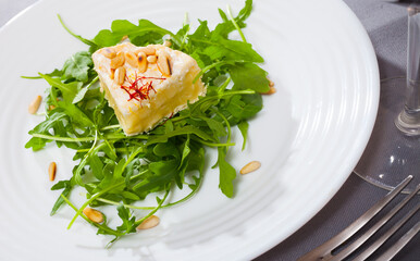 Quarter of camembert cheese on pillow with fresh arugula and toasted pine nuts on white plate