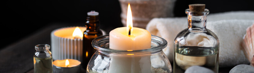 Spa setting with essential oil, candle, sea salt, pebbles, towel on dark wooden background. Massage, aromatherapy. Natural organic ingredients for relaxation, detention, wellness. Banner copy space