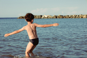 6 year old boy from behind playing in water on the shore of a sea. Vacation concept. 