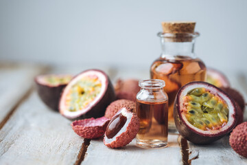 Glass bottles with pure organic essential litchi and passion fruit oil on wooden background. Concept of natural ingredients for beauty treatment, skin care, massage. Exotic fruits extract and essence - obrazy, fototapety, plakaty