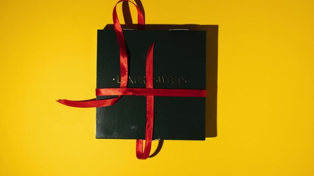 Stop motion animation of packing homemade multicolored chocolate bonbons in a gift box tied with a red ribbon. Flat lay. Assortment of hand painted candies. Chocolatier products on yellow background.