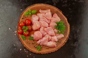 Chicken fillet.Fresh pieces of turkey meat.Raw chicken.Close up.Raw pieces of turkey meat with herbs and tomatoes on a wooden board on a black background.Ogranic food and healthy eating.