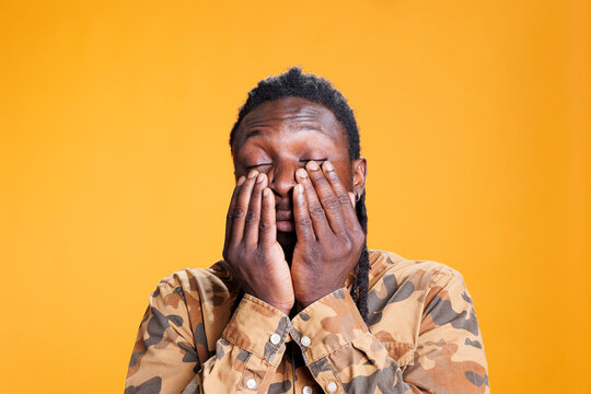 Tired overworked young adult having exhausted expression, being stressed in studio over yellow background. Frustrated african american man feeling overworked and sleepy, trying to be awake.