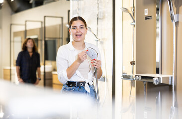 Positive young woman choosing a shower head in a hardware store