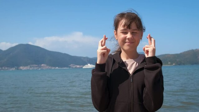 Hoping child with cross fingers on beach. A view of hopefull young girl cross her fingers on the summer beach. A concept of dreaming teen during traveling.
