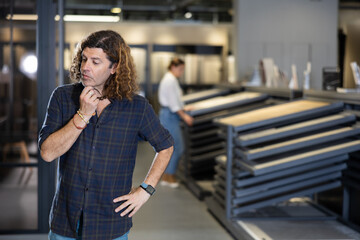 Fototapeta premium in hardware store, wistful man reflects on price-quality ratio of presented options for parquet flooring