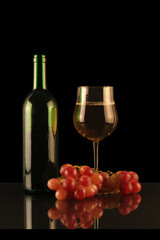 bottle and glass of white wine with grapes on a black background