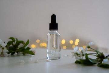 Clear glass cosmetic dropper bottle and white cherry flowers with bokeh lights, care product mockup, faded colors