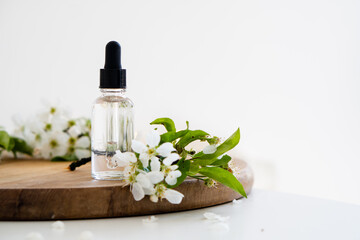 Obraz na płótnie Canvas Clear glass cosmetic dropper bottle and white cherry flowers on wooden board, care product mockup