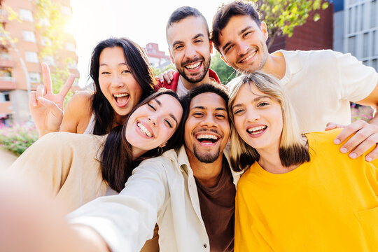 Happy group of diverse millennial friends taking selfie portrait together using mobile phone app. Multi ethnic teenage people having fun in city street. Friendship and youth lifestyle concept