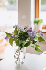 Bouquet of garden lilacs in a glass vase on a table and sunny light.