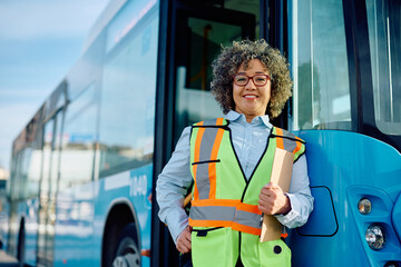 Happy female driver with clipboard at bus station looking at camera. © Drazen