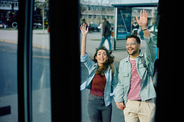 Young couple running with raised hands while trying to catch bus at station.