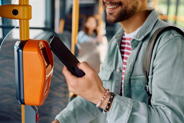 Close up of commuter validating card with smart phone while onboarding in bus