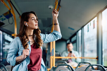 Young pensive woman listens music over earbuds while riding in bus.