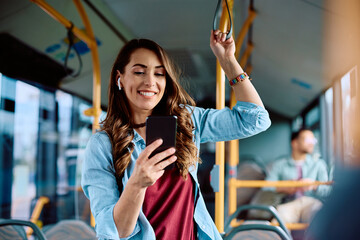 Happy woman using smart phone while commuting by bus.
