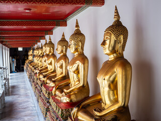 Golden Buddha statues in a long line along a wall at the Wat Pho Temple in Bangkok, Thailand.