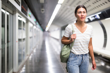 Woman with shoulder bag waiting for subway train in metro station.