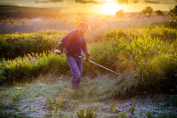 man mowing a lawn with lawn mower at sunset