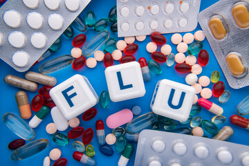 colorful pill and cubes with the inscription - FLU. On the blue table Medicine concept.