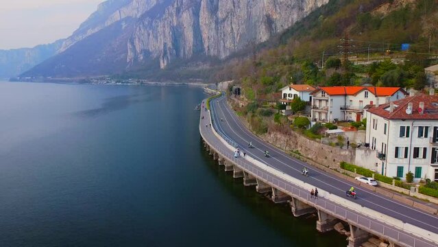 Aerial view of a beautiful european city near the shore of freshwater lake como in lombardy. Gothic church bell tower. Roofs of buildings. Mountains and rocks. Road by the water. Lecco Italy 11.2023