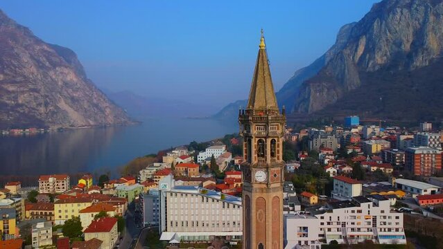 Aerial view of a beautiful european city near the shore of freshwater lake como in lombardy. Gothic church bell tower. Roofs of buildings. Mountains and rocks. Road by the water. Lecco Italy