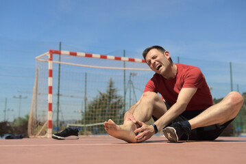 Sprain twisted ankle. Futsal sport injury. Male touching foot in pain due to swollen and broken...