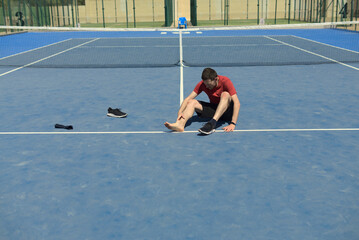wide angle view of man wearing red t-shirt in a blue tennis court, shoe is off. He has swollen...