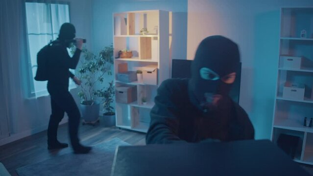 A Two Thieves in Black Clothes and a Mask Broke Into an Apartment or House. A Criminals in the Night with a Flashlight Finds a TV and Hacking the Safe and Then Running. Real-Time Video Surveillance