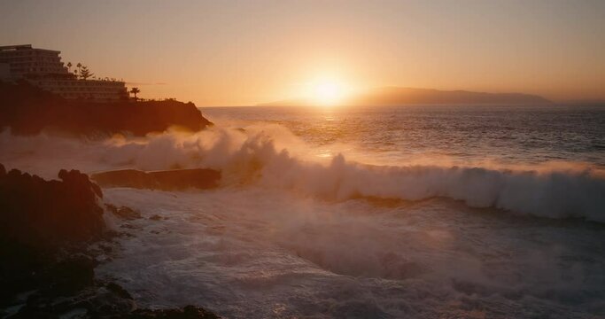 Slow-motion raging ocean waves crashing on rocks at sunset. Storm rough sea water at dusk. Sun goes below the horizon.