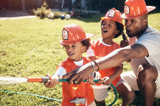 Father playing with his sons outside. Little boys dressed as firemen. African American boys playing outside. Brothers playing with a hosepipe in the garden. Siblings spraying water from a hosepipe.