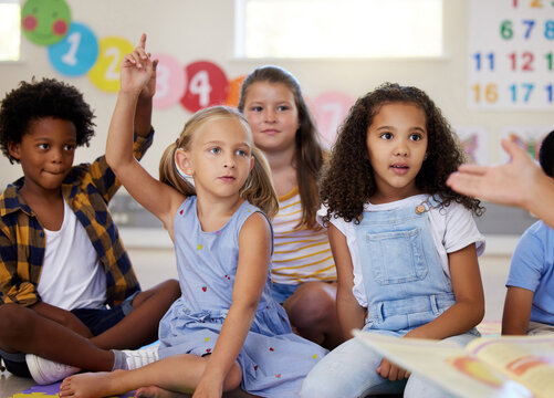 We learn a lot through reading. Shot of little kids raising their hands in class.