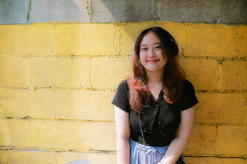 portrait of asian young woman standing against yellow wall with sunlight and shade with smiling face