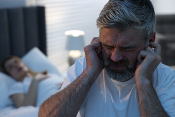 Irritated man covering his ears in bed at home, space for text. Problem with snoring wife