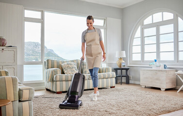 Freshening up her home. Shot of a young woman vacuuming a carpet in the lounge at home.