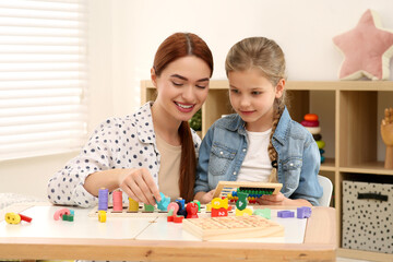 Fototapeta premium Happy mother and daughter playing with different math game kits at desk in room. Study mathematics with pleasure