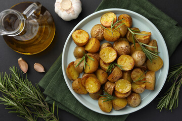 Fototapeta na wymiar Delicious baked potatoes with rosemary and ingredients on black table, flat lay