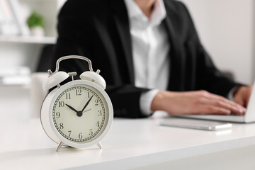 White alarm clock and man working at table in office, closeup with space for text. Deadline concept